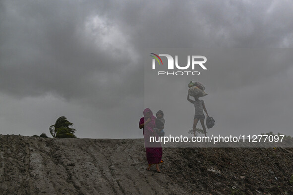 A woman with her child and a man with his belongings are walking towards a shelter during a rainfall in Kuakata, Bangladesh, on May 26, 2024...