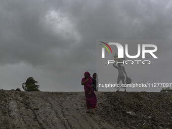 A woman with her child and a man with his belongings are walking towards a shelter during a rainfall in Kuakata, Bangladesh, on May 26, 2024...