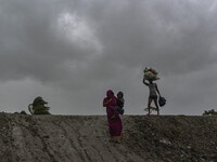 A woman with her child and a man with his belongings are walking towards a shelter during a rainfall in Kuakata, Bangladesh, on May 26, 2024...