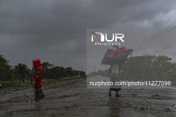 People with their belongings are walking towards a shelter during a rainfall in Kuakata, Bangladesh, on May 26, 2024, ahead of cyclone Remal...