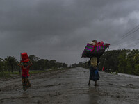 People with their belongings are walking towards a shelter during a rainfall in Kuakata, Bangladesh, on May 26, 2024, ahead of cyclone Remal...