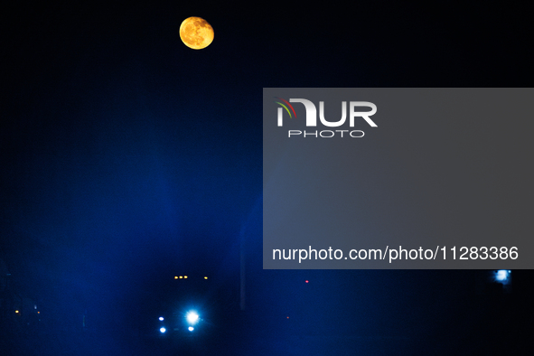 The glare from a semi-trailer truck's headlight is seen through haze under a nearly full moon as it travels on Highway 277 in Eagle Pass, Te...