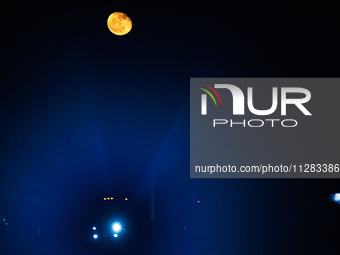 The glare from a semi-trailer truck's headlight is seen through haze under a nearly full moon as it travels on Highway 277 in Eagle Pass, Te...