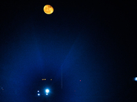 The glare from a semi-trailer truck's headlight is seen through haze under a nearly full moon as it travels on Highway 277 in Eagle Pass, Te...