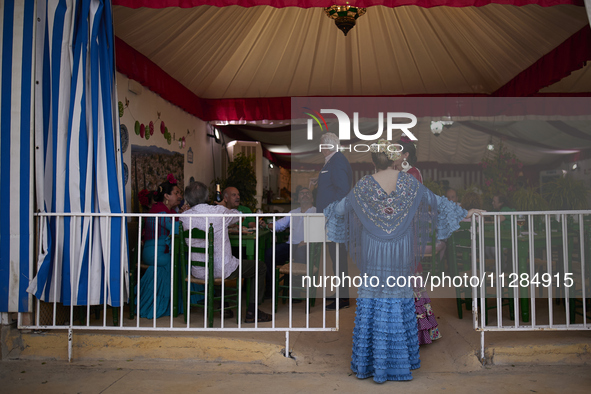 A woman dressed in a typical flamenco dress is talking to other people at the entrance to a ''caseta'' during the festivities of the Corpus...