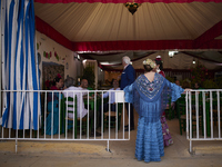 A woman dressed in a typical flamenco dress is talking to other people at the entrance to a ''caseta'' during the festivities of the Corpus...