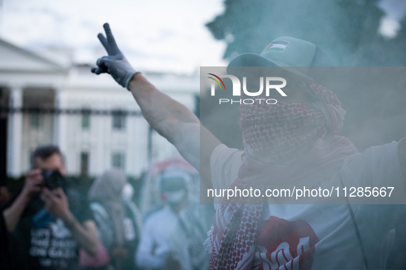 A demonstrator stands in front of a green smoke canister in front of the White House during a protest against the Israeli attacks on civilia...