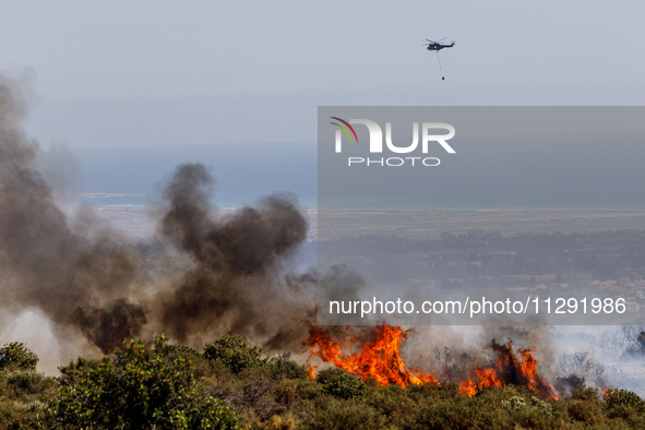 A helicopter is flying above the flames in Limassol, Cyprus, on May 31, 2024. Some buildings are in danger after a fire breaks out in the Ag...