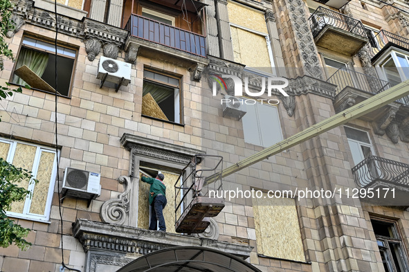 A municipal worker is using an aerial work platform to seal a smashed window with a particle board at a residential building damaged by the...