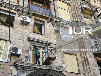 A municipal worker is using an aerial work platform to seal a smashed window with a particle board at a residential building damaged by the...