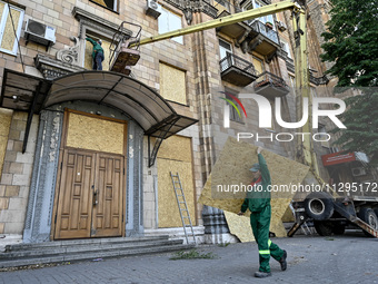 A municipal worker is carrying a particle board to seal a smashed window at a residential building damaged by the Russian missile attack in...