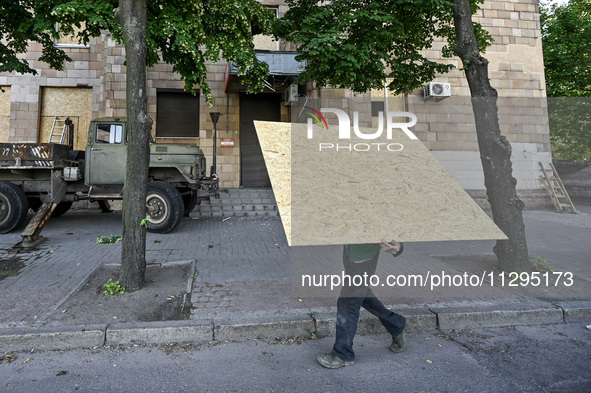 A municipal worker is carrying a particle board to seal a smashed window at a residential building damaged by the Russian missile attack in...