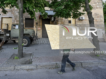 A municipal worker is carrying a particle board to seal a smashed window at a residential building damaged by the Russian missile attack in...