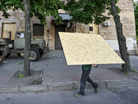 A municipal worker is carrying a particle board to seal a smashed window at a residential building damaged by the Russian missile attack in...