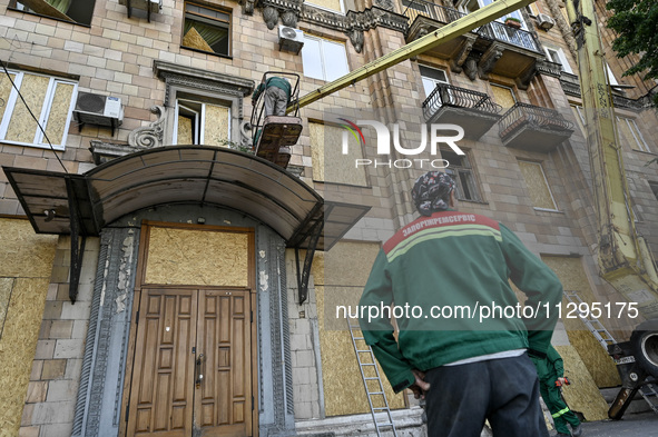 A municipal worker is using an aerial work platform to seal a smashed window with a particle board at a residential building damaged by the...