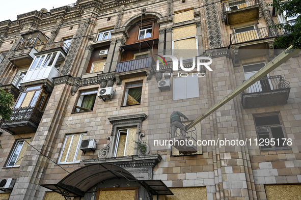 A municipal worker is using an aerial work platform to seal a smashed window with a particle board at a residential building damaged by the...