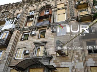 A municipal worker is using an aerial work platform to seal a smashed window with a particle board at a residential building damaged by the...