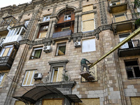 A municipal worker is using an aerial work platform to seal a smashed window with a particle board at a residential building damaged by the...