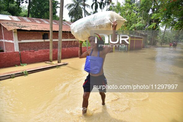 A man is carrying his belongings as he is walking through a flooded road in the aftermath of Cyclone Remal, in Nagaon district of Assam, Ind...