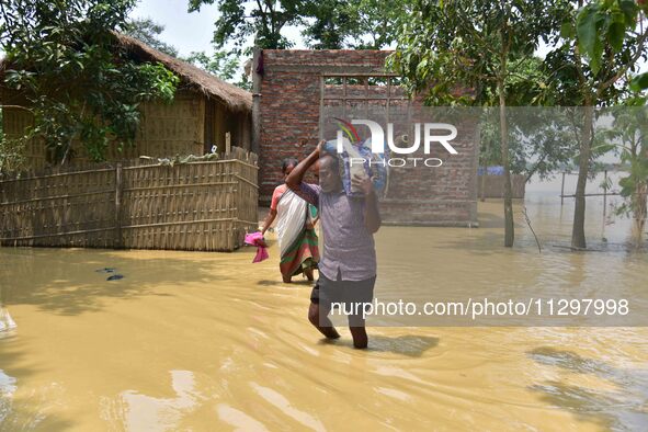 A man is carrying his belongings as he is walking through a flooded road in the aftermath of Cyclone Remal, in Nagaon district of Assam, Ind...