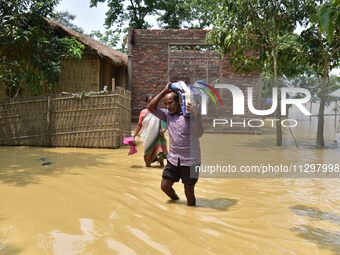 A man is carrying his belongings as he is walking through a flooded road in the aftermath of Cyclone Remal, in Nagaon district of Assam, Ind...