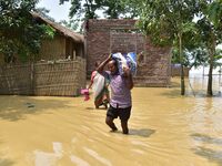 A man is carrying his belongings as he is walking through a flooded road in the aftermath of Cyclone Remal, in Nagaon district of Assam, Ind...