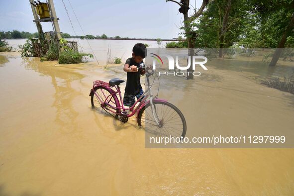 A boy is pushing his bicycle as he is walking through a flooded road following rains in the aftermath of Cyclone Remal, in Nagaon district o...