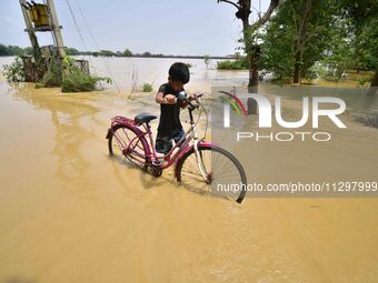 A boy is pushing his bicycle as he is walking through a flooded road following rains in the aftermath of Cyclone Remal, in Nagaon district o...