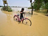 A boy is pushing his bicycle as he is walking through a flooded road following rains in the aftermath of Cyclone Remal, in Nagaon district o...