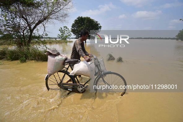 A man is pushing his bicycle as he walks through a flooded road following rains in the aftermath of Cyclone Remal, in Nagaon district of Ass...