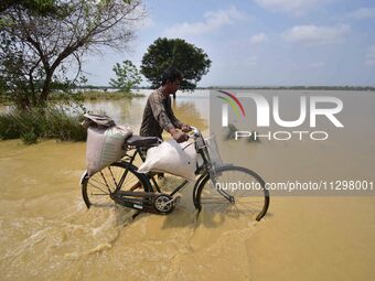 A man is pushing his bicycle as he walks through a flooded road following rains in the aftermath of Cyclone Remal, in Nagaon district of Ass...