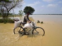 A man is pushing his bicycle as he walks through a flooded road following rains in the aftermath of Cyclone Remal, in Nagaon district of Ass...