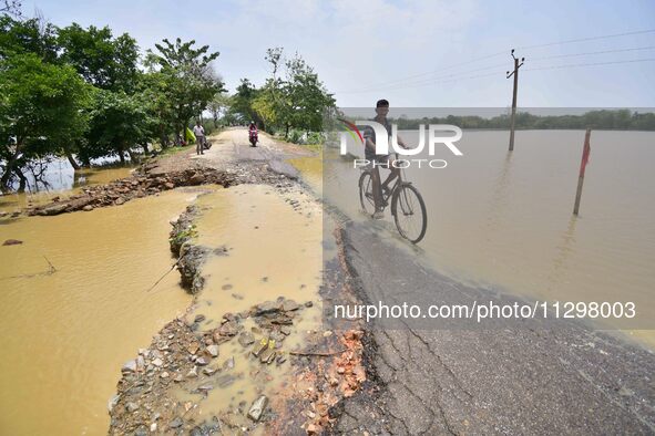 A man is riding his bicycle on a road damaged by flood following rains in the aftermath of Cyclone Remal, in Nagaon district of Assam, India...