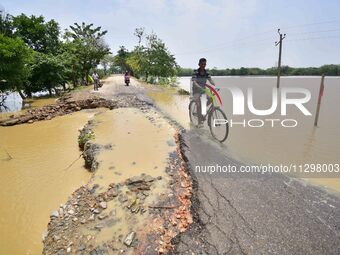 A man is riding his bicycle on a road damaged by flood following rains in the aftermath of Cyclone Remal, in Nagaon district of Assam, India...