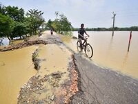 A man is riding his bicycle on a road damaged by flood following rains in the aftermath of Cyclone Remal, in Nagaon district of Assam, India...