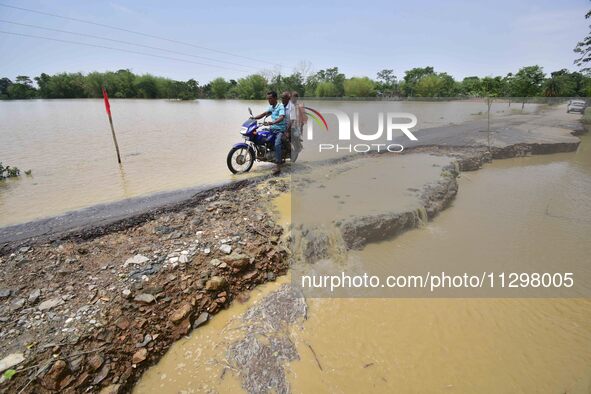 A man is riding a bike on a road damaged by flood following rains in the aftermath of Cyclone Remal, in Nagaon district of Assam, India, on...