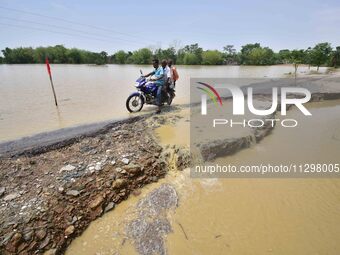 A man is riding a bike on a road damaged by flood following rains in the aftermath of Cyclone Remal, in Nagaon district of Assam, India, on...