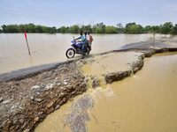 A man is riding a bike on a road damaged by flood following rains in the aftermath of Cyclone Remal, in Nagaon district of Assam, India, on...