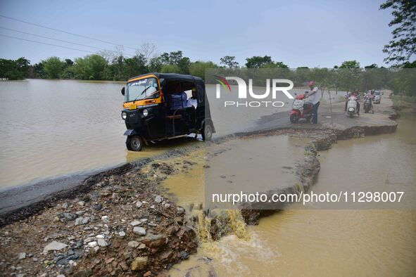 People are riding three-wheelers on a road damaged by flood following rains in the aftermath of Cyclone Remal, in Nagaon district of Assam,...