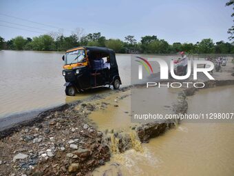 People are riding three-wheelers on a road damaged by flood following rains in the aftermath of Cyclone Remal, in Nagaon district of Assam,...