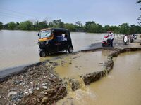 People are riding three-wheelers on a road damaged by flood following rains in the aftermath of Cyclone Remal, in Nagaon district of Assam,...