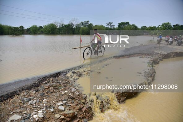 A man is riding his bicycle on a road damaged by flood following rains in the aftermath of Cyclone Remal, in Nagaon district of Assam, India...