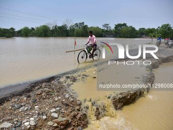 A man is riding his bicycle on a road damaged by flood following rains in the aftermath of Cyclone Remal, in Nagaon district of Assam, India...