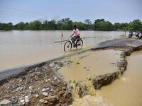 A man is riding his bicycle on a road damaged by flood following rains in the aftermath of Cyclone Remal, in Nagaon district of Assam, India...