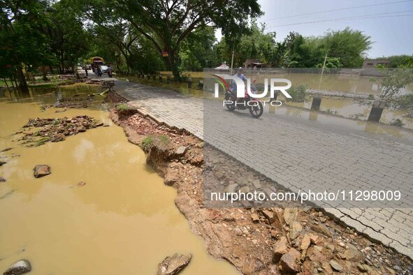 A man is riding his bike on a road damaged by flood following rains in the aftermath of Cyclone Remal, in Nagaon district of Assam, India, o...