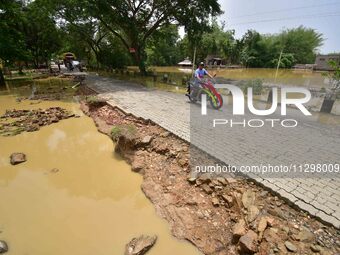 A man is riding his bike on a road damaged by flood following rains in the aftermath of Cyclone Remal, in Nagaon district of Assam, India, o...