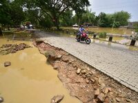 A man is riding his bike on a road damaged by flood following rains in the aftermath of Cyclone Remal, in Nagaon district of Assam, India, o...