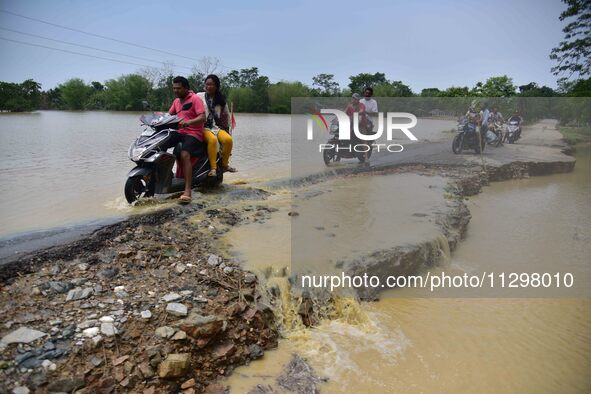 People are riding two-wheelers on a road damaged by flood following rains in the aftermath of Cyclone Remal, in Nagaon district of Assam, In...