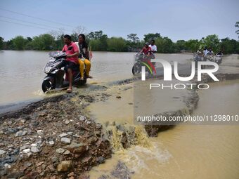 People are riding two-wheelers on a road damaged by flood following rains in the aftermath of Cyclone Remal, in Nagaon district of Assam, In...