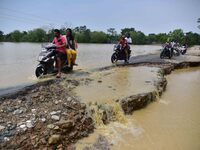 People are riding two-wheelers on a road damaged by flood following rains in the aftermath of Cyclone Remal, in Nagaon district of Assam, In...